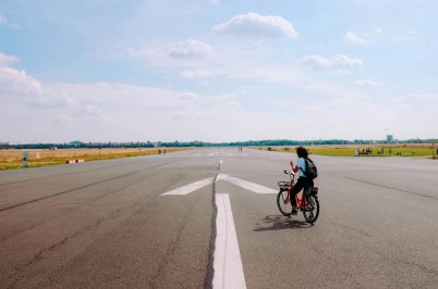 A cyclist enjoys a leisurely ride on an airport runway under a clear blue sky, highlighting peaceful outdoor urban life.