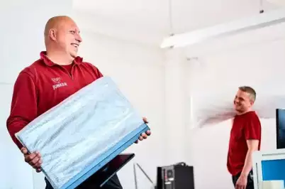 Zwei Mitarbeiter der Umzugsfirma Junker transportieren Computerbildschirme und Verpackungsmaterial bei einem Büro-Umzug